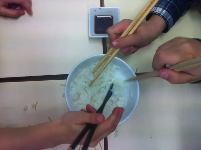 In the image we can see there is a bowl in which there is a rice and people are holding chopsticks...