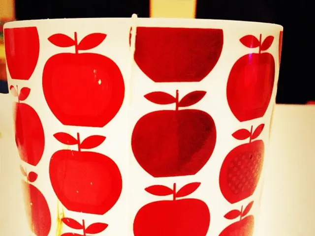 In the image there is a cup that has apple images on it and there is a tea bag kept inside the cup.