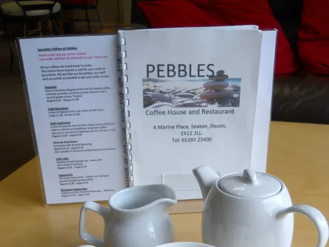 In this image I can see few teapot, cup, saucer and spoon. I can see few white papers on the stand....