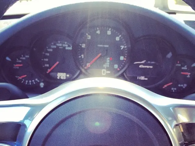 In this image we can see the speedometer and steering of the Porsche car.