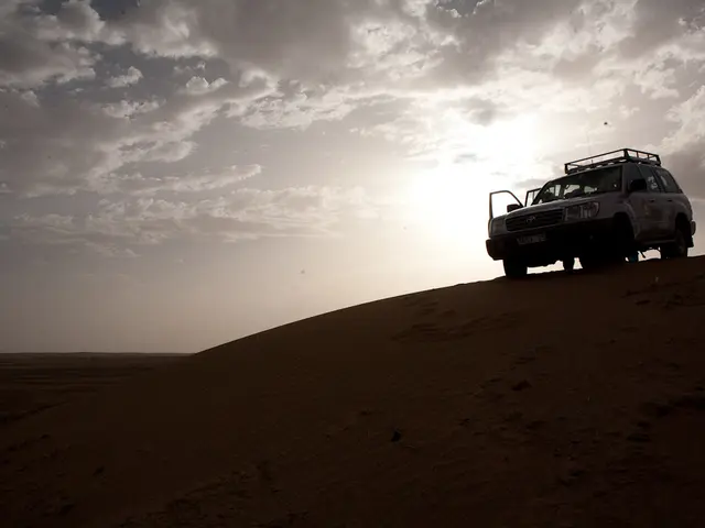 In this image there is a vehicle on the land. Top of image there is sky with some clouds.